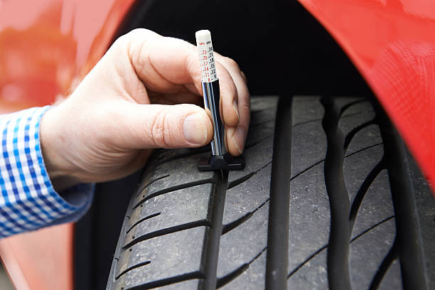 Close-Up Of Man Checking Tread On Car Tyre With Gauge stock photo