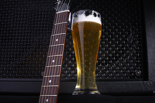 Tall glass full of light beer standing near a grilled music monitor with a guitar fretboard in the foreground