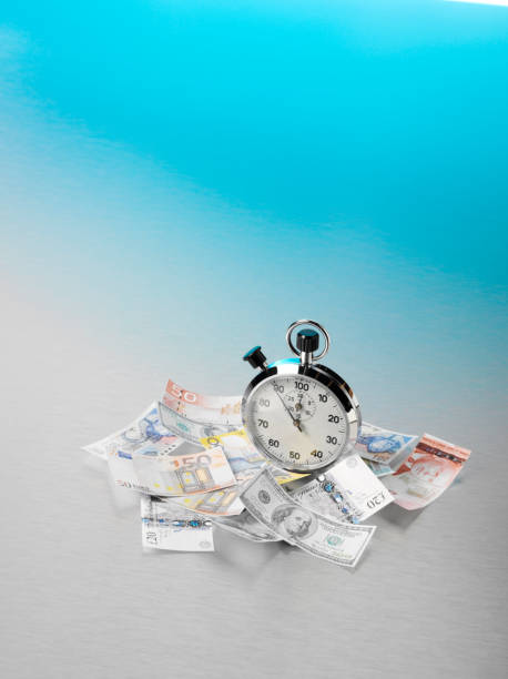 American, European and British Currency Scattered Around a Stopwatch American, European and British currency scattered around a stopwatch, with copy space on a stainless steel background with blue lighting. Time is money concept. twenty pound note stock pictures, royalty-free photos & images