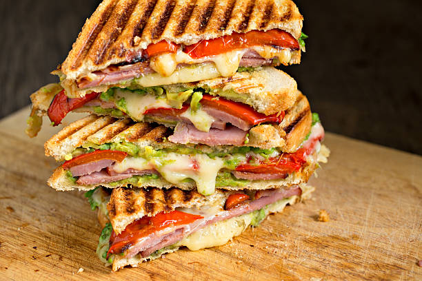 Stack Of Ham And Cheese  Sandwiches An extreme close up shot of a stack of grilled ham, avocado and cheese grilled panini sandwiches on a cutting board panino stock pictures, royalty-free photos & images