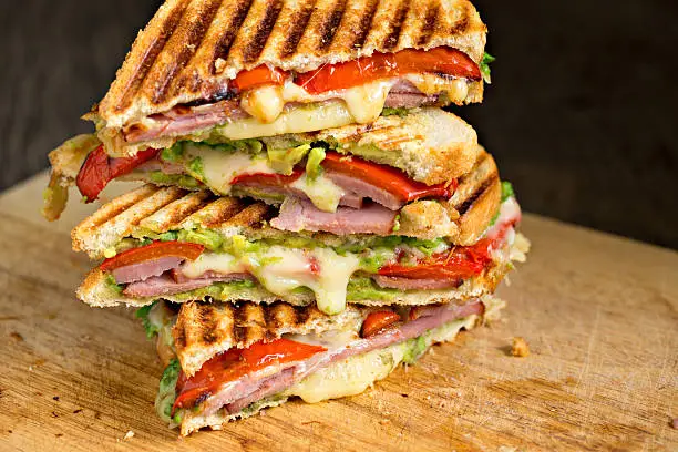 An extreme close up shot of a stack of grilled ham, avocado and cheese grilled panini sandwiches on a cutting board