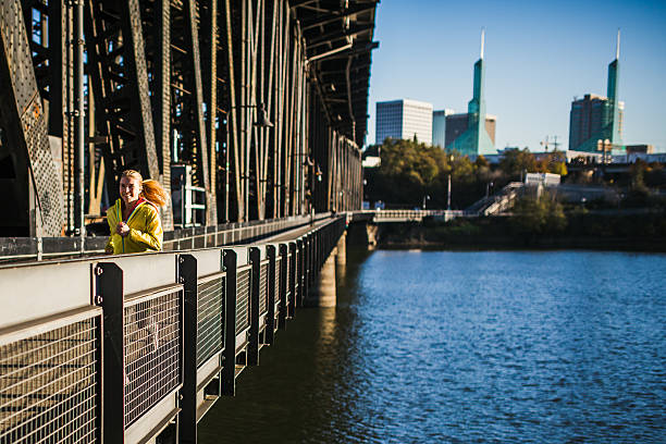 A young athletic woman goes for a morning jog, running along the foot / bike traffic path on the Broadway bridge over the Willamette River in Portland, Oregon.  Horizontal image with copy space.
