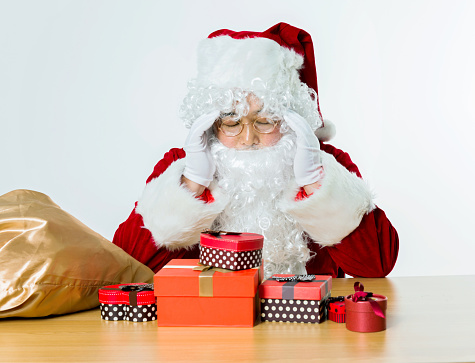 Tired santa claus with group of gifts on desk.