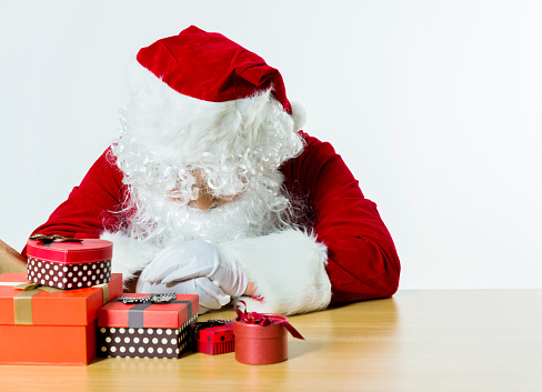 Tired santa claus with group of gifts on desk.
