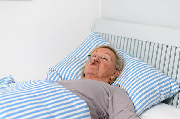 istock Sick Woman Lying on Bed with Thermometer in Mouth 477211376