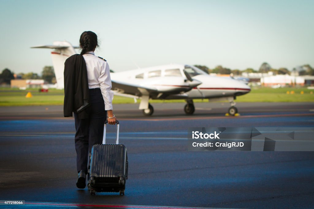 Pilot Departing A female pilot walks towards her aircraft. She has her uniform on, jacket over the shoulder, and is pulling a suitcase. Pilot Stock Photo