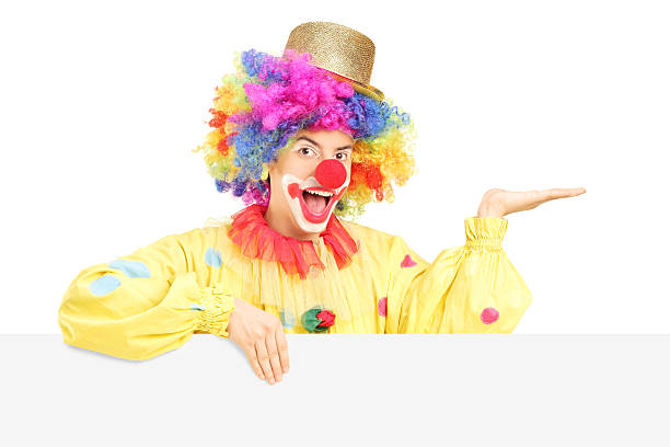 istock Smiling male clown standing behind blank panel gesturing with hand 477222627