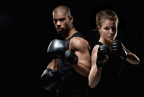 Two fighters, one black male and one white female, posing with raised fists on a black background