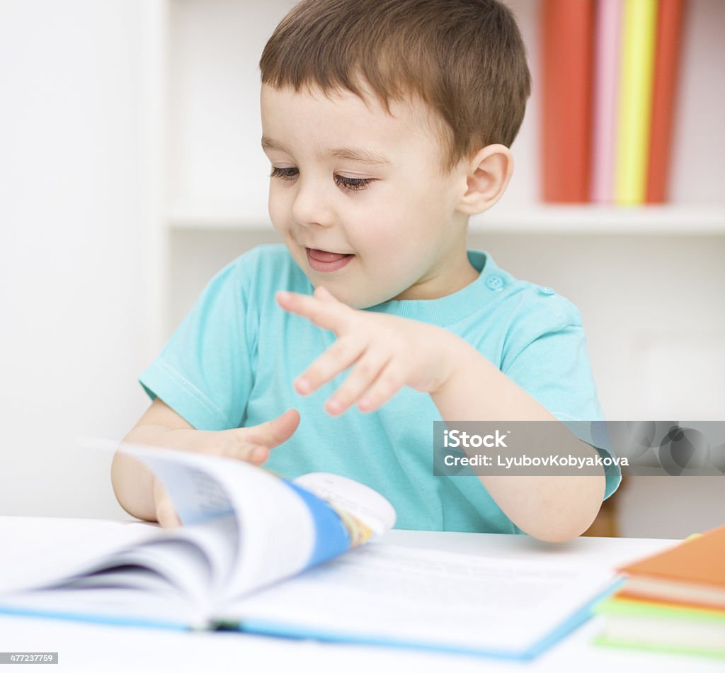 Little boy is reading a book Cute little boy is reading book while sitting at table, indoor shoot Book Stock Photo