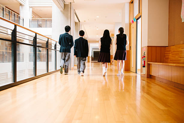 Japanese high school. Four students walk through corridor, rear view A view of a Japanese high school. Four students walk through a corridor, rear view. Unrecognisable, contemporary architecture, interior view, horizontal composition. japanese boy and girl stock pictures, royalty-free photos & images