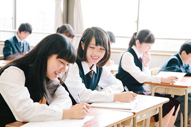 High school students, teenagers study happily in a classroom, Japan High school students, seven teenagers study in a classroom, Japan. Interior shot, sitting and writing at a desk, young people, in a row, horizontal composition. Focus on the foreground. japanese boy and girl stock pictures, royalty-free photos & images