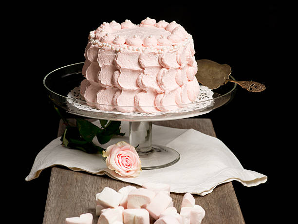 istock Scalloped pale pink cake on glass stand next to rose. 477254113