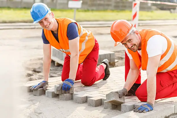 Two smiling construction workers laying new cobblestones