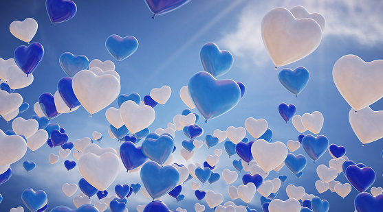 A group of heart-shaped balloons raising upwards on a cloudy sky background. The hearts appear bright in a blue and white color and have a slightly marbled surface.