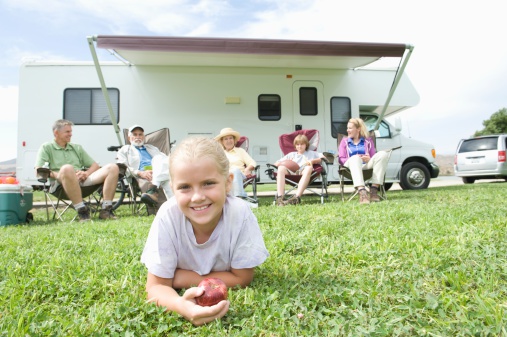 Portrait of a cute little girl lying on grass with family sitting outside RV home