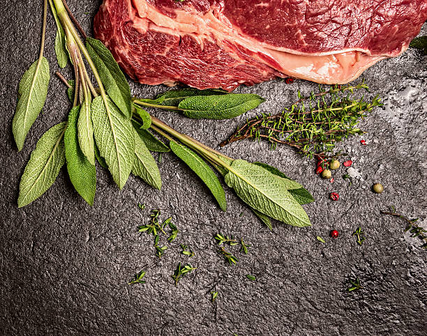 Beef meat with sage and thyme on black stone background