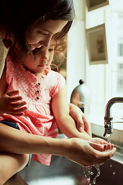 Mother and daughter washing hands in kitchen