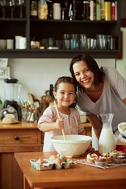 portrait of smiling mother and daughter while baking in kitchen