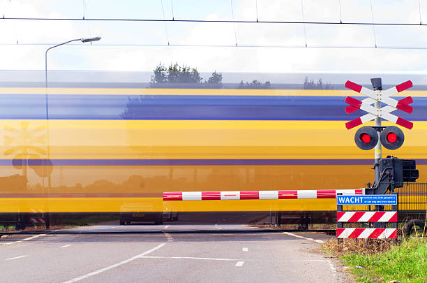 On a foggy morning along this transition of the track with barrier and lights, a passenger train rages by