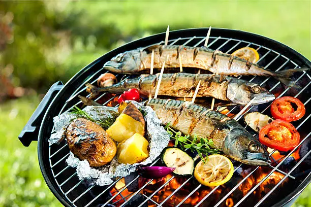Grilled mackerel fish with baked potatoes over the coals on a barbecue