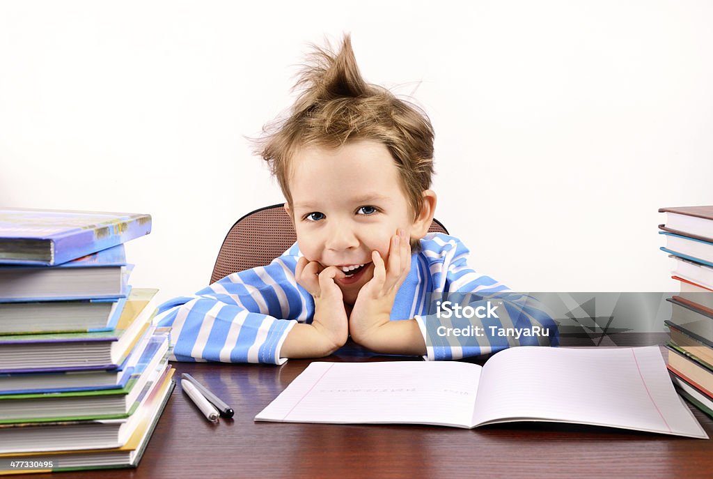 cute boy laughing sitting at the desk cute boy laughing sitting at the desk. many textbooks on the desk. light background.  horisontal Boys Stock Photo