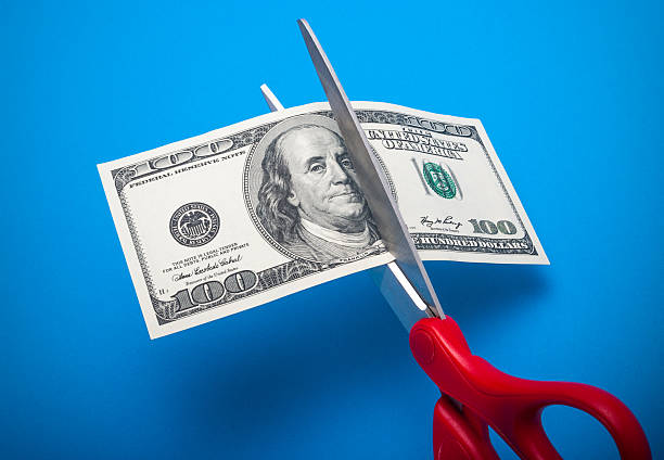 Cutting costs 100 dollar bill being cut with scissors isolated on a blue background cutting stock pictures, royalty-free photos & images
