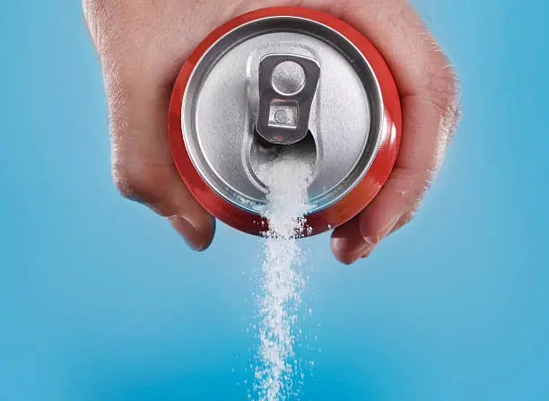 hand holding soda can pouring a crazy amount of sugar in metaphor of sugar content of a refresh drink isolated on blue background in healthy nutrition, diet and sweet addiction concept