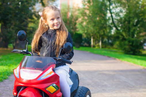 Portrait of happy little rock girl in leather jacket sitting on her toy motorcycle