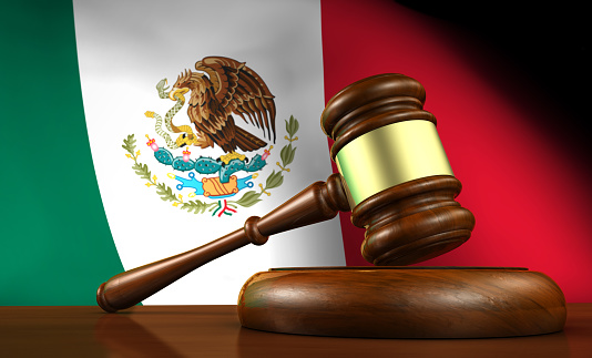 Law and justice of Mexico concept with a 3d rendering of a gavel on a wooden desktop and the Mexican flag on background.