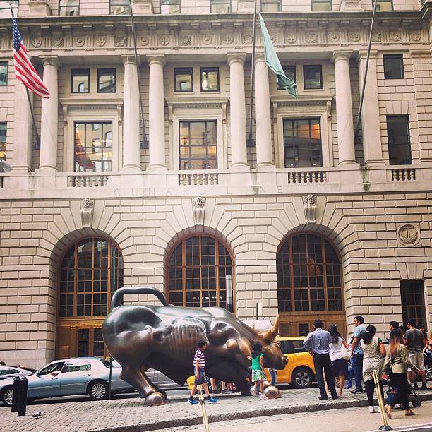 New York, New York, USA - May 28, 2015: Charging Bull of Wall Street Statue located on Broadway, Downtown New York City. With people gathered around the sculpture. Image taken with mobile phone. 
