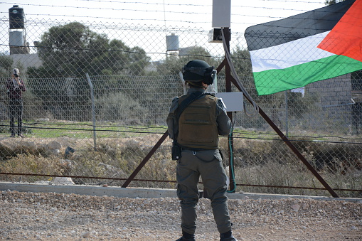 Jerusalem, Israel – November 16, 2014: Israeli soldier stand next to the Palestine flag at the separation barrier. 