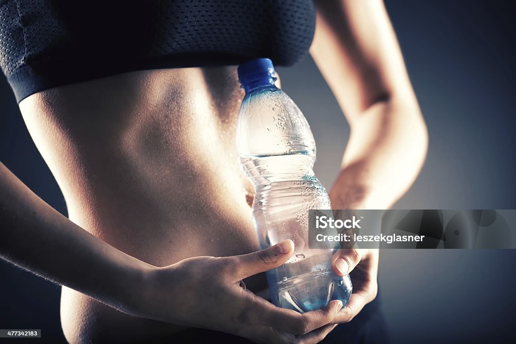 Sweaty mujer sosteniendo una botella de agua después de capacitación - Foto de stock de Abdomen libre de derechos