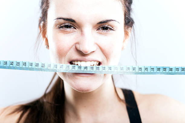 istock Angry young woman biting measuring tape 477343827