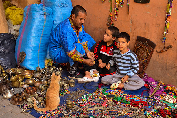 Marrakesh, Morocco - November 14, 2012:  Moroccan father and sons having lunch as they sell their wares on the streets of Marrakesh.  A stray cat watches and waits patiently for a hand out.