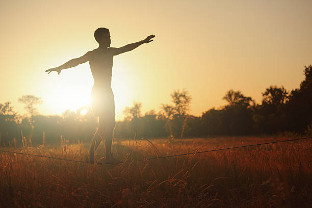 Man walking on slackline in the meadow at sunset.