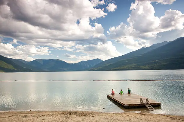 Photo of Three People Sitting on Dock at Mountain Lake