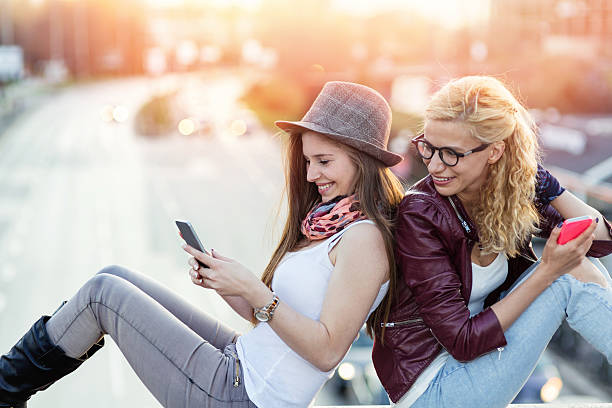 istock Two girls using cell phones in the city 477384356