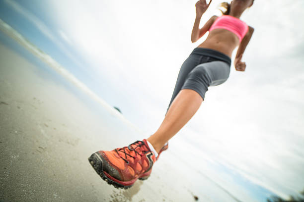 Young woman jogging on the beach on a cloudy day. Low angle view.