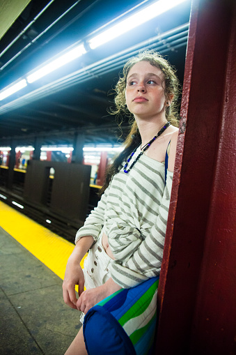Tired teenager girl and other unrecognized people at the subway platform at trainstation. USA, New York City, New York.