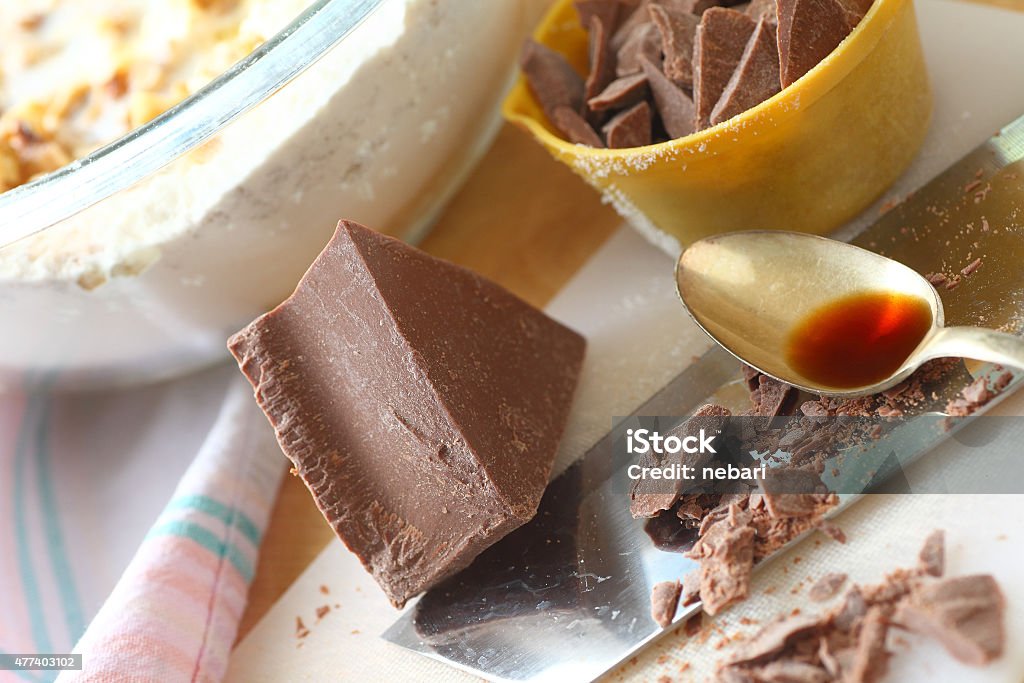 Chopped chocolate and tablespoon of vanilla Block of chocolate, some chopped in measuring cup, with vanilla, and mixing bowl of batter 2015 Stock Photo