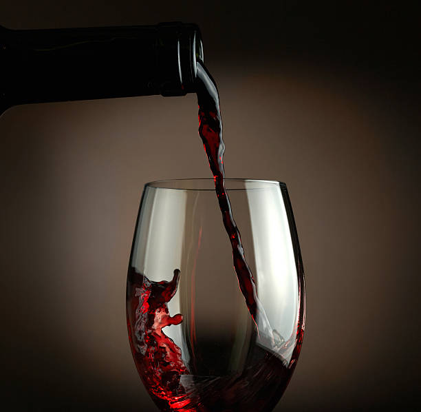 istock Red wine pouring into glass over dark background 477407319