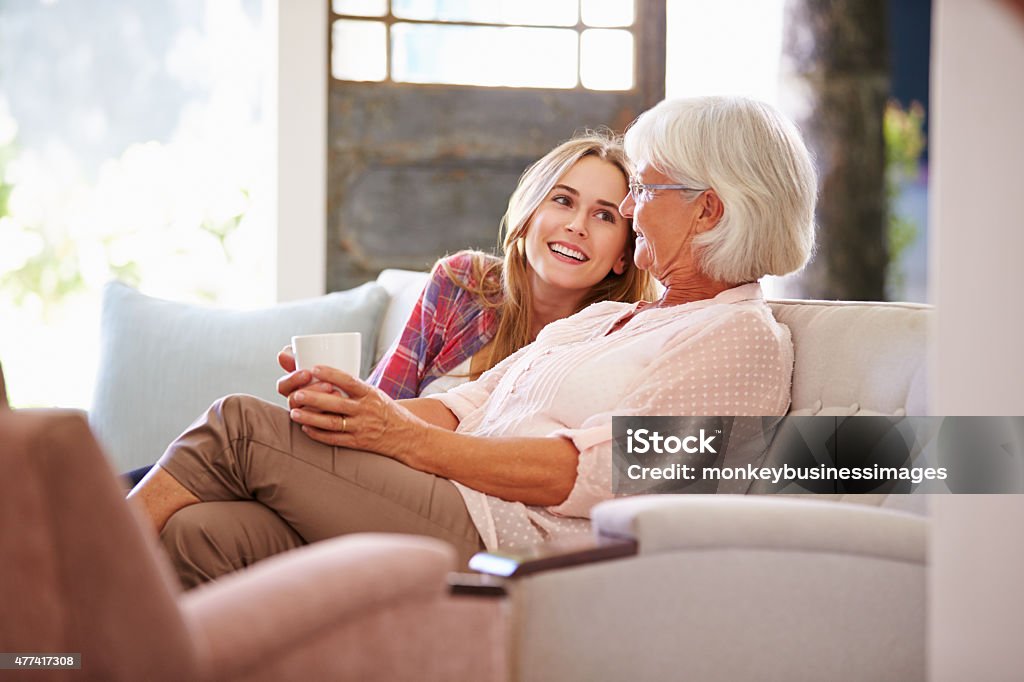 Grandmother With Adult Granddaughter Relaxing On Sofa Grandmother Stock Photo