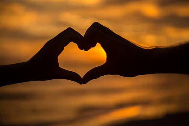 istock Silhouette of hands on beach at sunset making heart shape. 477420112