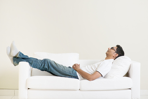 Indian guy daydreaming and rest at home. Asian man relaxed and sleep on sofa indoor. Handsome male model.