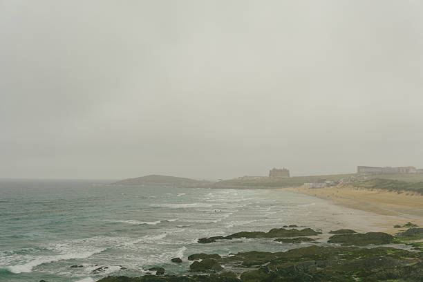 A gloomy June day overlooking Fistral Beach, Newquay, Cornwall . . . very fine drizzle fills the sky. A few Surfers and people on the beach.