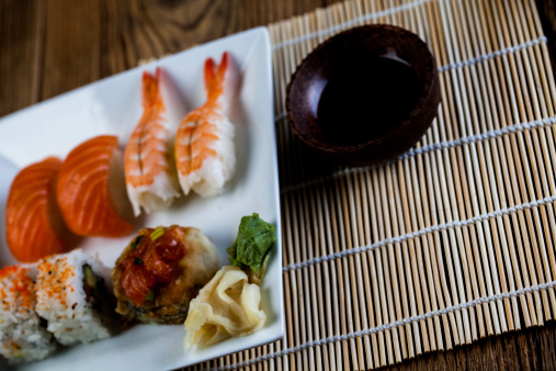 Close up on a plate with arranged sessame seed and seaweed sushi rolls placed on a wooden table.