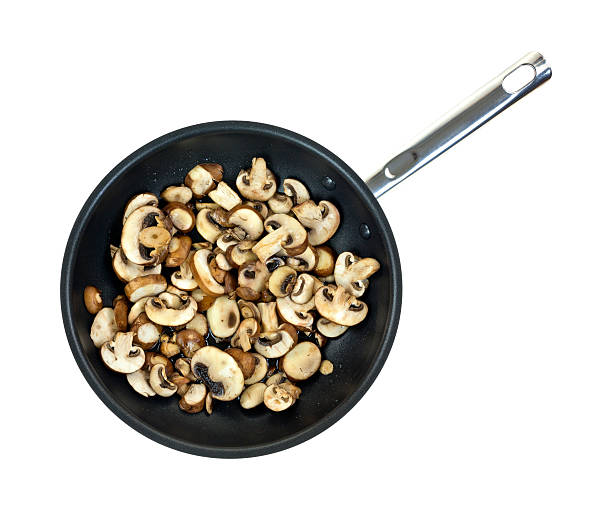 Top view of mushrooms sauteing in olive oil in a large skillet on a white background.