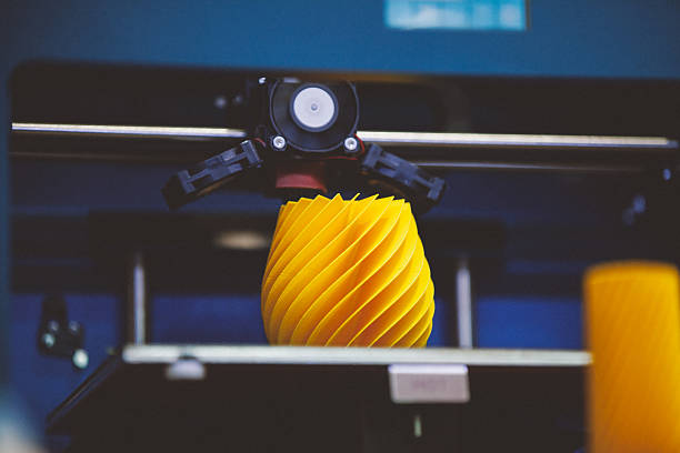 3D printing machine detail in action Blue three dimensional printer working creating a yellow plastic object. 3d printing photos stock pictures, royalty-free photos & images