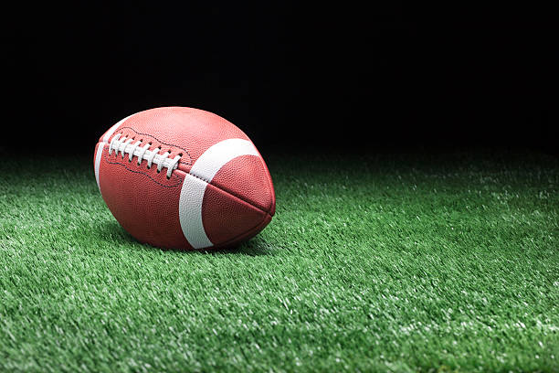 Football on grass against dark background College style football on grass field against dark background american football field photos stock pictures, royalty-free photos & images