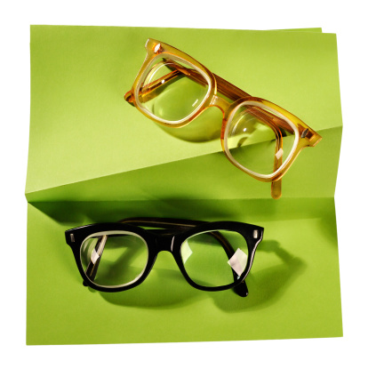 Retro eyeglasses with black frame and yellow frame on creative support made of green paper, photographed on white background. The image is clear, sharp and can be easily customized.